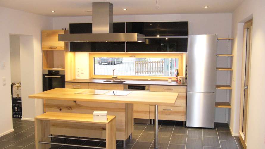 Zweizeilige Küche mit freistehender Kochinsel in Buche mit schwarzem Glas in den Oberschränken und einem Fenster in der Nische 